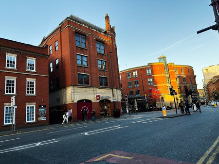 Manchester, UK - November 17, 2025: Busy Manchester street scene featuring brick buildings, storefronts, and people crossing at traffic lights during daytime.のeditorial素材