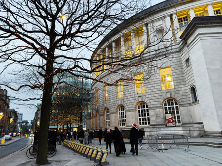 Manchester, UK - December 10, 2025: Evening in Manchester UK with a lit classical facade, tree lights, and passersby in winter attire.のeditorial素材
