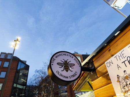 Manchester, UK - December 10, 2025: Circular bee logo sign advertising The Manchester Shop on a wooden market stall in Manchester, UK.のeditorial素材