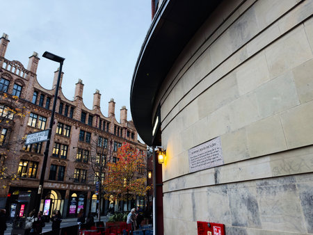 Manchester, UK - December 10, 2025: Bustling Manchester street scene with historic brick buildings, autumn trees, and a curved modern facade.のeditorial素材