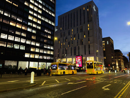 Manchester, UK - December 10, 2025: Bustling night scene in Manchester featuring yellow buses, tall offices, and illuminated streets.のeditorial素材