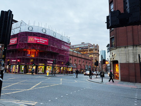Manchester, UK - December 10, 2025: Urban shopping street in Manchester with scaffolded renovation, glowing storefronts, and people crossing at street.のeditorial素材