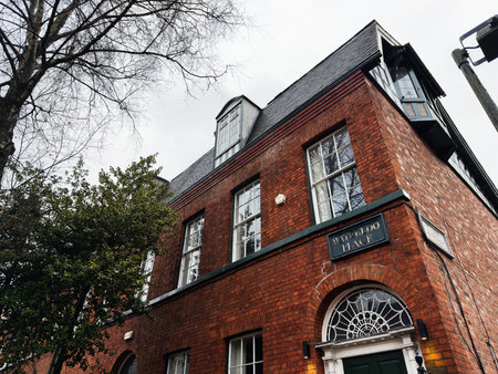 Manchester, UK - December 06, 2025: A Manchester urban facade with red brick, timeless architecture, arched doorway, and tree-lined street.のeditorial素材