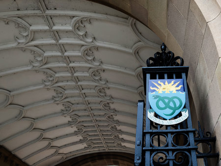 Manchester, UK - December 06, 2025: Decorative crest with sun and intertwined emblem on an iron gate...
