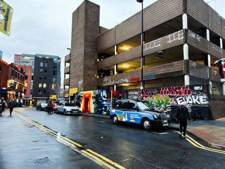 Manchester, UK - December 01, 2025: Urban scene in Manchester featuring graffiti art, a blue taxi,...