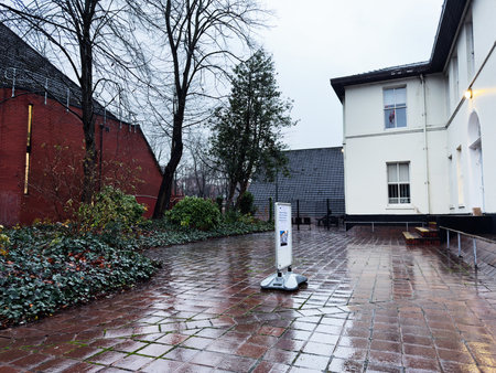 Manchester, UK - December 06, 2025: A wet outdoor scene in Manchester featuring a white building, brick wall, trees, and signage.のeditorial素材
