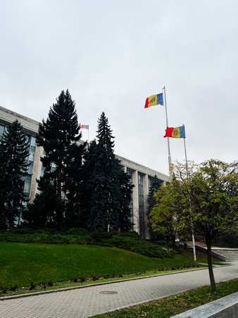 Chisinau, Moldova - November 29, 2025: Flags fly beside a government building with trees, a manicured lawn, and a paved path under an overcast sky in Chisinau, Moldova.のeditorial素材