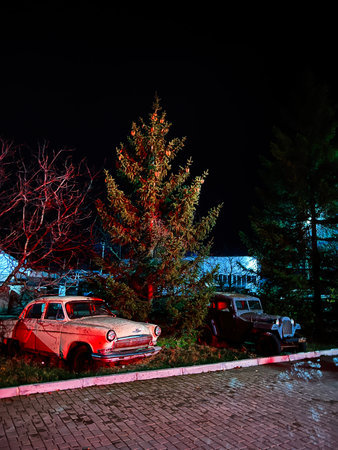 Basarabeasca, Moldova - November 29, 2025: Night scene with vintage vehicles beside a pine tree in a quiet, moody lot in Basarabeasca, Moldova.のeditorial素材
