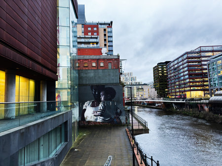 Manchester, UK - January 21, 2026: A vibrant Manchester city scene with a canal, glass buildings, and a large mural.のeditorial素材