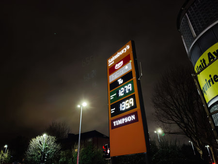 Manchester, UK - January 21, 2026: Night scene in Manchester shows a tall orange price board with fuel prices beside Sainsbury's sign and Timpson storefront at street level.のeditorial素材