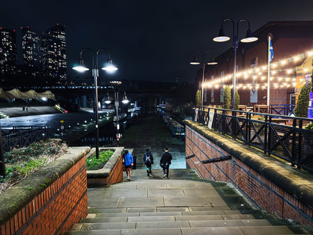 Manchester, UK - January 21, 2026: Night scene in Manchester showing brick stairs, canal path, and illuminated strings above a lively riverside.のeditorial素材