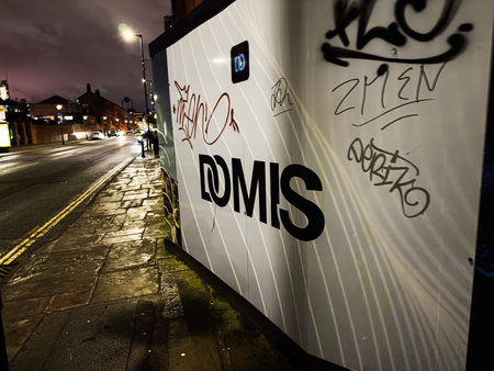 Manchester, UK - January 21, 2026: Graffiti covered DOMIS panel on a Manchester street at night, urban vibe and graffiti art.のeditorial素材