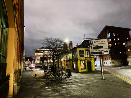 Manchester, UK - January 21, 2026: Moody evening in Manchester featuring a bright pub, bikes, signs, and city lights.のeditorial素材