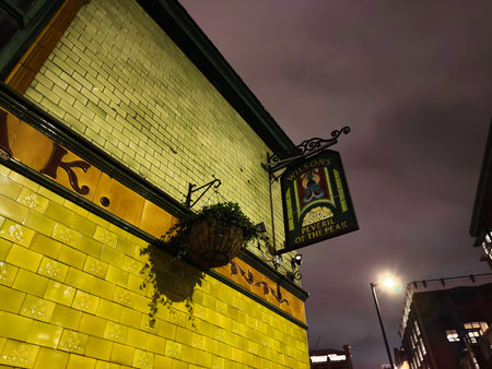 Manchester, UK - January 21, 2026: Warm night scene of a yellow tiled Peveril of the Peak pub exterior in Manchester featuring a hanging sign and plant.のeditorial素材