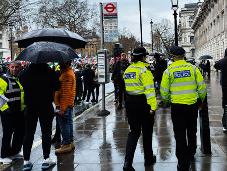 London, UK - February 01, 2026: Crowd and police guard a rainy London street during an Iranian opposition rally, umbrellas up and tense atmosphere.のeditorial素材