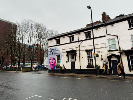 Manchester, UK - January 22, 2026: A rainy Manchester street featuring a colorful mural, pedestrians, and a white historic building.のeditorial素材