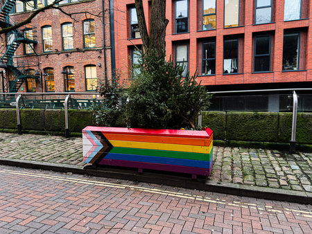 Colorful rainbow LGBTq planter with a small evergreen tree along a cobblestone path beside red brick buildings in Manchester, UK.のeditorial素材