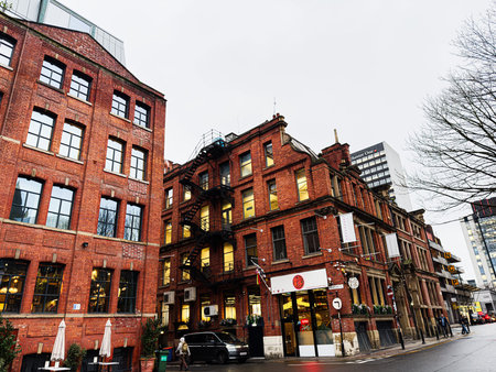 Manchester, UK - January 22, 2026: Urban scene in Manchester with red brick buildings, storefronts,...
