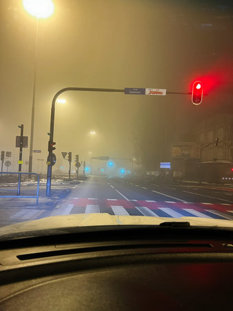 Mist and street lamps illuminate a lone urban intersection as red signal glows under fog.の写真素材