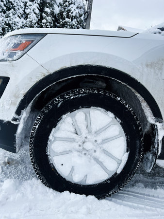 White car wheel and snow covered tire in a cold winter setting with snow on ground.