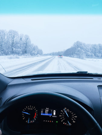 View from the car dashboard as winter snow covers the road and frost outlines the trees.