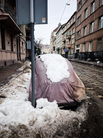 Covered vintage car in snow on a quiet urban street with tram tracks and snow piled along the curb.の写真素材