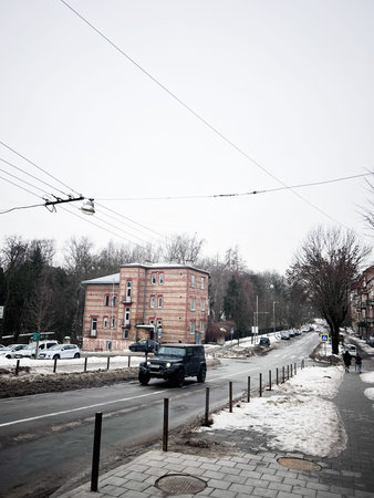 Lviv, Ukraine - February 07, 2026: Snowy urban street with brick apartment building, parked cars, and overhead power lines on a cold day.のeditorial素材