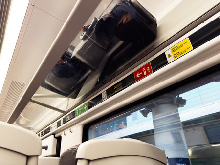 Interior of a train carriage shows overhead luggage, safety signs, and seated passengers in a calm setting.の写真素材