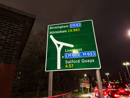 Night highway sign in Manchester guiding drivers to Birmingham Altrincham Liverpool and Salford...