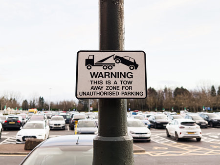 A warning sign attached to a pole in a busy Manchester parking lot, indicating tow away for...