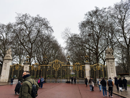 London, UK - February 01, 2026: Visitors stroll past an elaborate gold and black gate in London, framed by bare trees and overcast skies.のeditorial素材