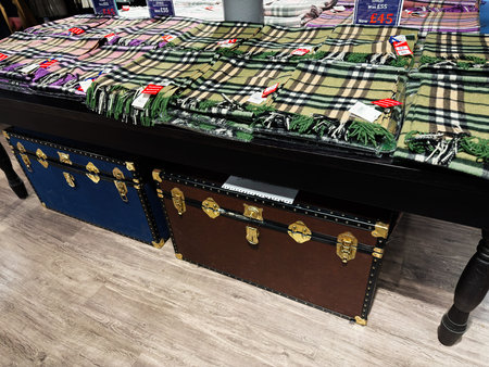 Edinburgh, Scotland, UK - February 15, 2026: Tartan wool scarves neatly folded on a display table above leather travel trunks in an Edinburgh boutique.のeditorial素材