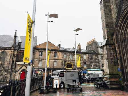 Edinburgh, Scotland, UK - February 15, 2026: Outdoor coffee trailer and picnic benches beside historic stone buildings and festival banners in rainy Old Town Edinburgh.のeditorial素材