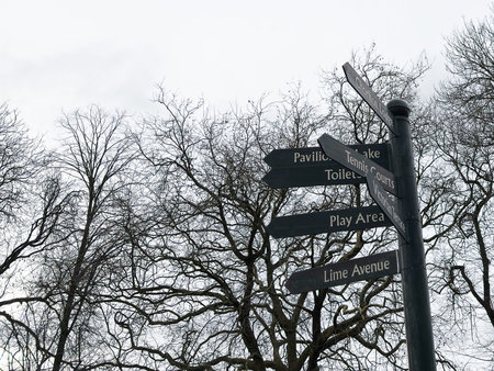 Dark directional sign points to Lime Avenue and play areas against leafless trees in Alexandra Park...