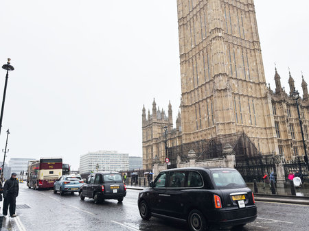 London, UK - February 01, 2026: Wet street traffic with iconic Big Ben tower, black cabs and buses...
