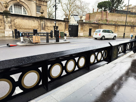 London street scene featuring a decorative railing, a white taxi, and brick walls along a wet...