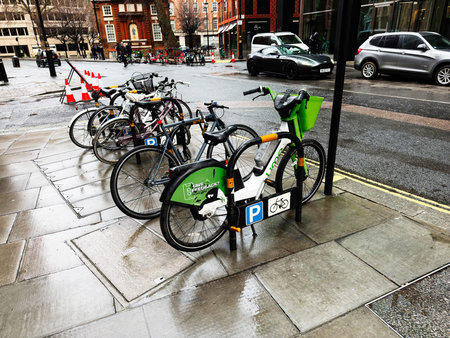 London, UK - February 01, 2026: Shared rental bicycles lined up at a wet city bike parking rack on a...