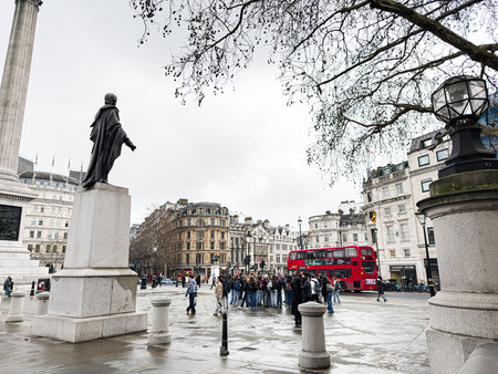 London, UK - February 02, 2026: Crowd of tourists gathers near a historic statue and red double-decker bus on wet Trafalgar Square in London, UK.のeditorial素材