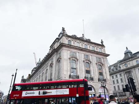 London, UK - February 02, 2026: A red double decker bus passes a grand neoclassical building on a busy London street with pedestrians.のeditorial素材