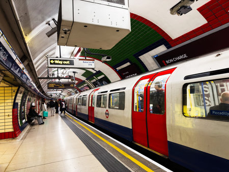 London, UK - February 02, 2026: Red and white London Piccadilly Circus Underground train at a tiled platform with commuters boarding and waiting.のeditorial素材