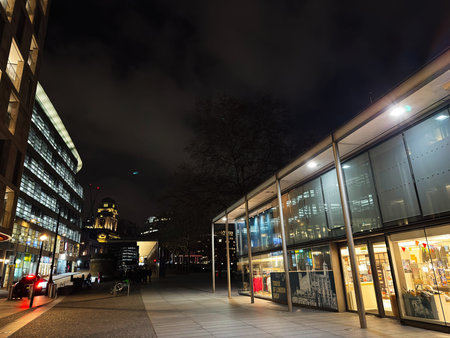 London, UK - February 02, 2026: Empty urban plaza at night featuring lit storefronts, office windows...