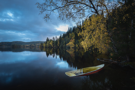 Wooden boat by the lake shore, Norway, beautiful autumn time, calm water. Old paddle boat in autumnal scenery.の写真素材