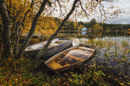 Wooden boat by the lake shore, Norway, beautiful autumn time, calm water. Old paddle boat in autumnal scenery.の写真素材