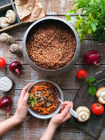 The girls hand puts buckwheat porridge from the pot into a plateの写真素材