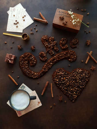 On a brown background there is a cup of coffee and coffee beans are scattered in the form of the word coffee and a heartの写真素材