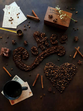 On a brown background there is a cup of coffee and coffee beans are scattered in the form of the word coffee and a heartの写真素材