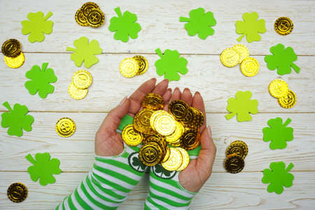 St. Patrick's Day. Woman's hands hold gold coins on a white wooden background.の写真素材