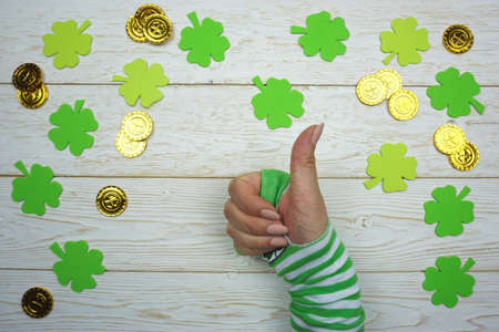 St. Patrick's Day. Hand with gold coins, clover leaves on a wooden background.
