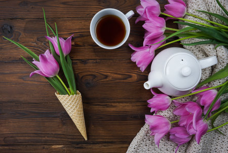 Tulips, a notebook, a white teapot and a cup of tea are laid out on a wooden tableの写真素材
