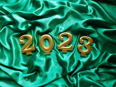 Candles in the form of numbers 2023 are lying on a silk green fabric